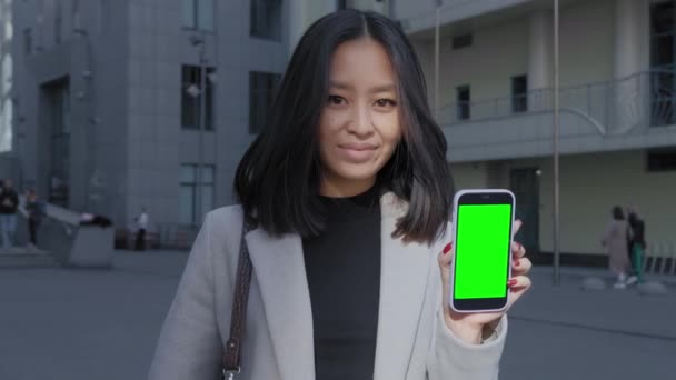 Asyalı iş kadını elinde yeşil ekran krom anahtarı olan akıllı bir telefon tutuyor. — Stok video