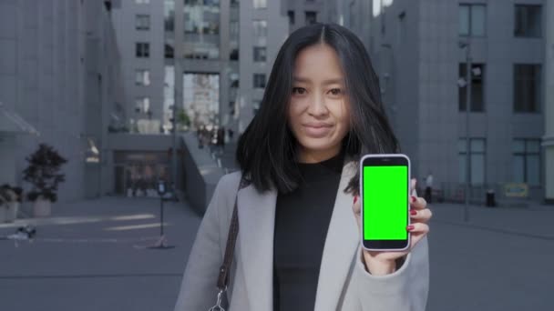 Mladý dospělý asijský student ukazuje chytrý telefon se zelenou obrazovkou chroma klíč ve městě — Stock video