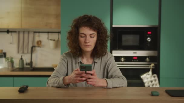 Jong twintiger jaren volwassen student typen op een telefoon in haar keuken — Stockvideo