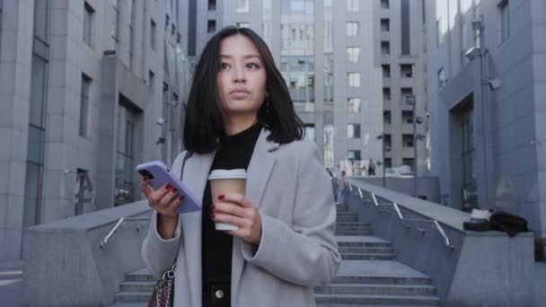 Retrato de una joven mujer de negocios asiática adulta mirando con un teléfono inteligente en sus manos — Vídeos de Stock