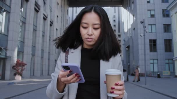 Asiatique femme d'affaires navigation sur son téléphone tout en marchant du bureau — Video