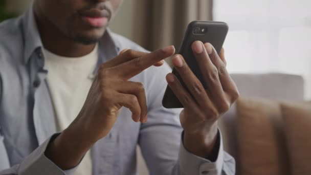 Primer plano de un irreconocible afroamericano joven adulto deslizando en un teléfono inteligente negro — Vídeos de Stock