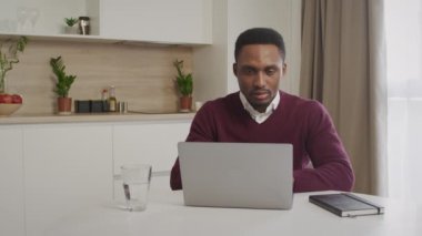 Afro-Amerikalı genç siyahi girişimci bilgisayarında mutlu ve sakin bir şekilde çalışıyor.