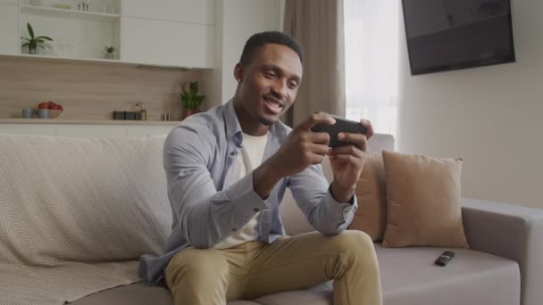 Feliz sorridente afro-americano jogando em seu telefone inteligente em seu apartamento — Vídeo de Stock