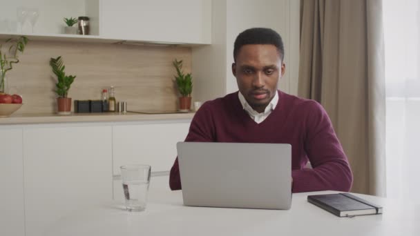 Afrikanischer junger schwarzer Unternehmer, der in seinem hellen Homeoffice glücklich und ruhig an seinem Laptop arbeitet — Stockvideo