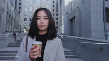 Şehir merkezindeki caddede elinde kahveyle genç ve güzel bir Asyalı kadının portresi.