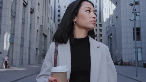 Close - up of a young adult asian businesswoman walking from office with a coffee cup in slow motion — Stock Video