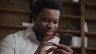 Genç siyahi bir adamın portresi, akıllı telefonuna bakarken başarıyı kutluyor.