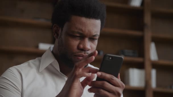 Närbild porträtt av en ung vuxen afrikansk man bläddrar på sin smartphone söker en lösning — Stockvideo