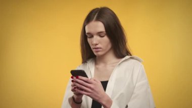 Genç, beyaz bir kadın, parlak sarı bir arka planda akıllı telefonuna cevap yazıyor.