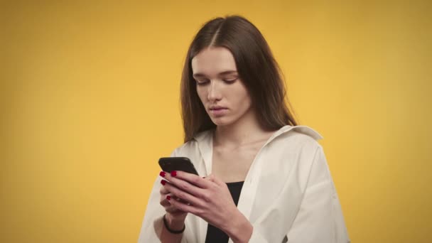 年轻的高加索女人在明亮的黄色背景下，用智能手机输入答案 — 图库视频影像