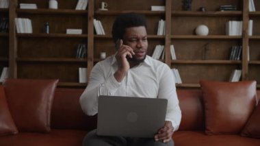 Genç yetişkin bir adam laptopuyla çalışırken telefonla kötü haber alıyor.