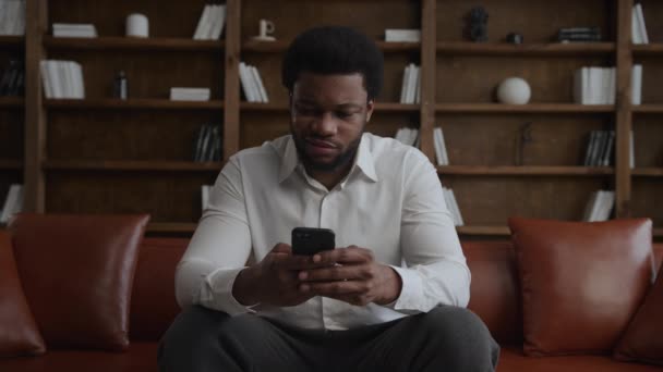Joven adulto afroamericano hombre no está contento con el precio, mientras que las compras en línea en su teléfono inteligente — Vídeo de stock