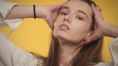 20 'li yaşlarda beyaz bir kadının parlak sarı bir arka planda kameraya gülümseyen portresi.