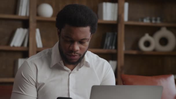 Joven hombre adulto respondiendo a una llamada telefónica delante de su portátil en ofiice — Vídeo de stock