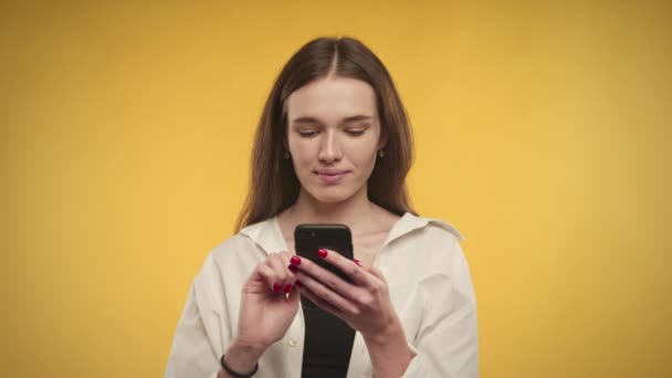 Jovem mulher caucasiana adulto é compras on-line em seu smartphone em um fundo amarelo brilhante — Vídeo de Stock