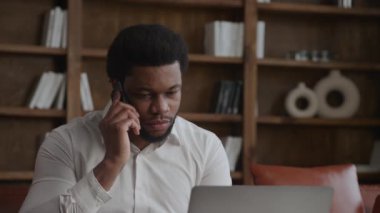 Ofis 'te genç bir adam laptopunun önünde telefona cevap veriyor.