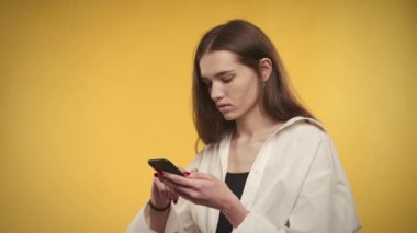 Genç, beyaz bir kadın, parlak sarı bir arka planda akıllı telefonuyla yapılan anlaşmaya şaşırır.