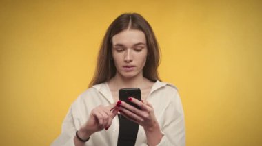 Genç beyaz kadın internet üzerinden akıllı telefondan parlak sarı arka planda alışveriş yapmayı düşünüyor.