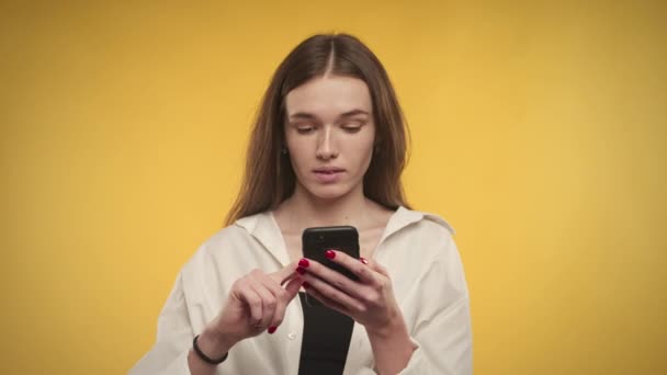 Jonge blanke vrouw is denken terwijl online winkelen op smartphone op heldere gele achtergrond — Stockvideo