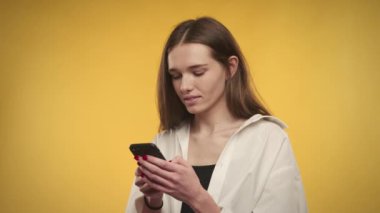 Kafkasyalı genç bir kadın, parlak sarı arka plandaki akıllı telefondan gelen mesaja şaşırır.