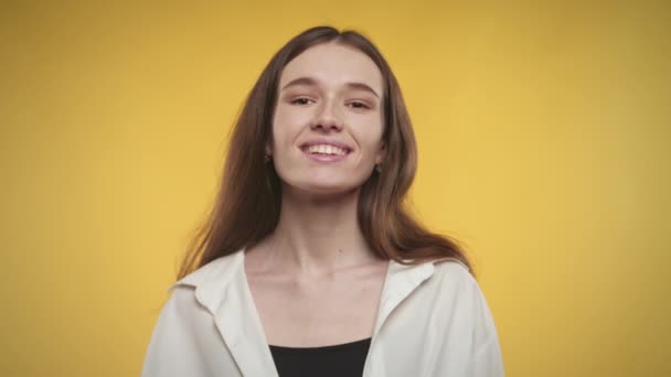 Junge erwachsene Kaukasierin blickt in die Kamera und lächelt auf leuchtend gelbem Hintergrund — Stockvideo