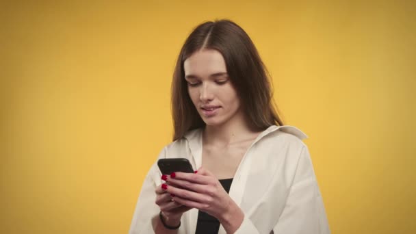 Jeune femme caucasienne adulte rit avec un smartphone dans les mains sur un fond jaune vif — Video