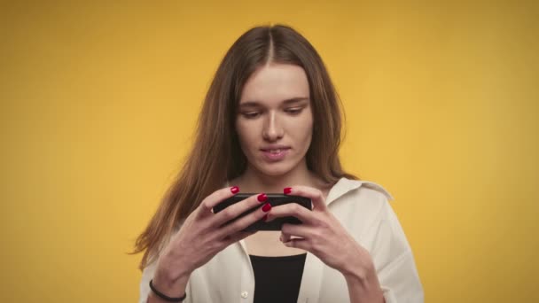 Молода доросла біла жінка виграє онлайн відеоігри на своєму смартфоні яскраво-жовтий фон — стокове відео