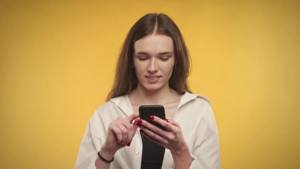 Молодая белая женщина на ярко-желтом фоне в студии надевает смартфон — стоковое видео