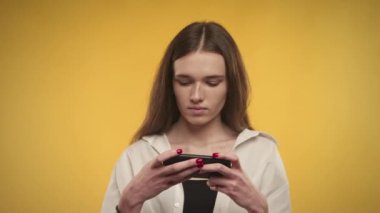 Genç beyaz kadın, parlak sarı bir arka planda akıllı telefonuyla oyun oynuyor.
