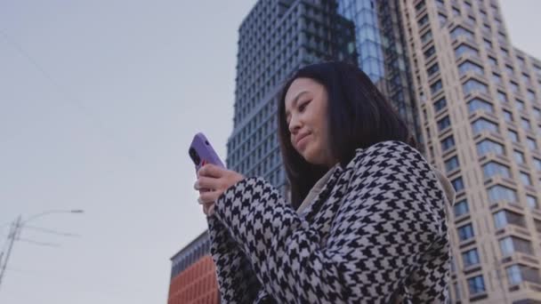 Lettura sul suo smartphone sotto il grattacielo della città — Video Stock