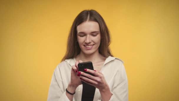 年轻的白人女性正在明亮的黄色背景下用智能手机打字 — 图库视频影像