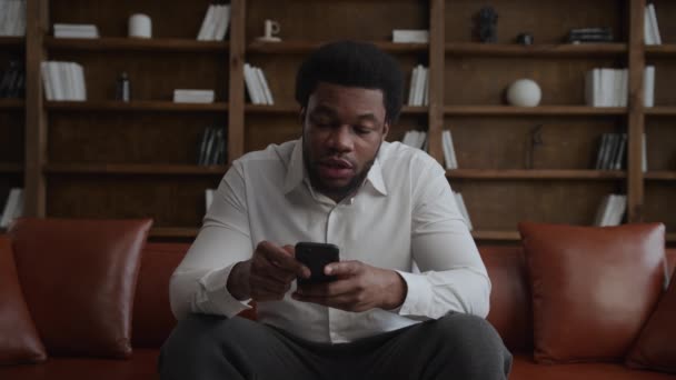 Genç, Afro-Amerikan bir adam. Çatı katında akıllı telefondan değişik yüz ifadeleriyle geziniyor. — Stok video