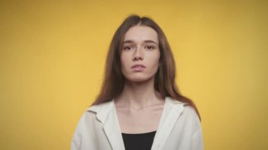 Kendine güvenen bir kadın, parlak sarı bir arka planda kameraya bakıyor.