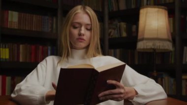 Yaşlı bir kütüphanede kitap okuyan genç bir kadın.