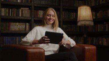 Beyaz saçlı genç bir kadın arkadaşlarıyla evde tablet kullanarak görüntülü konuşma yapıyor.