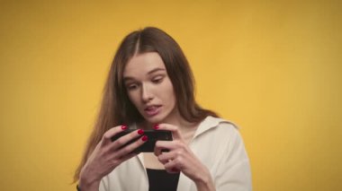 Genç bir kadın, parlak sarı bir arka planda akıllı telefonundan iyi haberler alıyor.