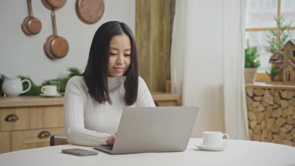 Joven mujer de 20 años es feliz mientras trabaja en su computadora portátil desde casa — Vídeos de Stock
