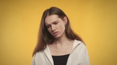 Genç beyaz kadın, parlak sarı bir arka planda mutsuz.