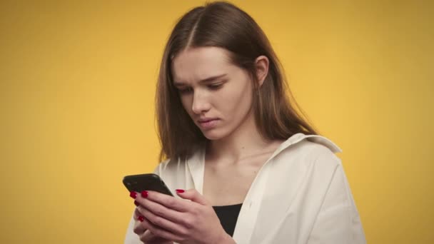 Jeune femme caucasienne adulte envoie des SMS sur son smartphone sur un fond jaune vif — Video