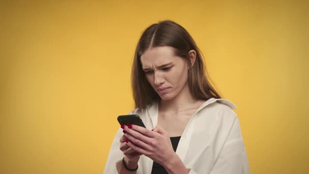 Νεαρή ενήλικη καυκάσια γυναίκα στέλνει μηνύματα στο smartphone της σε φωτεινό κίτρινο φόντο — Αρχείο Βίντεο