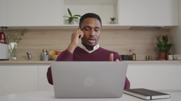 Joven hombre de negocios adulto que tiene una llamada en su teléfono delante de su computadora portátil — Vídeo de stock