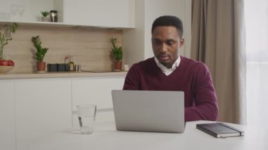 Afro-Amerikalı genç siyahi girişimci bilgisayarında mutlu ve sakin bir şekilde çalışıyor.