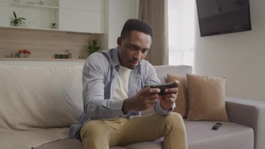 Konsantre olmuş genç Afrikalı Amerikalı yetişkin adam akıllı telefonuyla oyun oynuyor ve bu konuda heyecanlı.