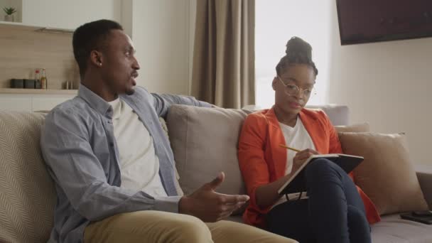 Psycholog nő hallgat egy fiatal felnőtt férfi és jegyzetel egy lakásban — Stock videók