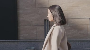 Asyalı bir iş kadınının şehir merkezinde yürüyüşünün yan görüntüsü