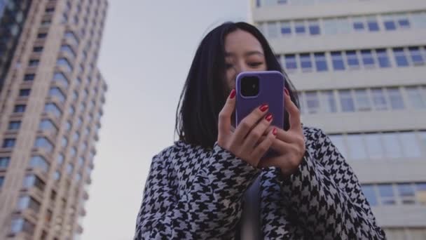 Mujer usando teléfono inteligente en la calle del centro de la ciudad bajo un edificio de gran altura — Vídeos de Stock