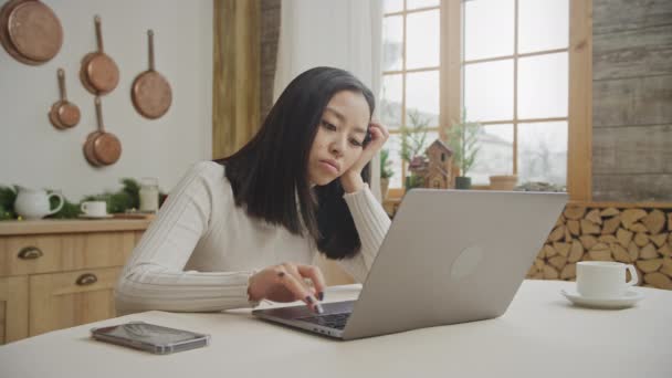 Mujer joven se aburre usando su computadora portátil en su apartamento cocina — Vídeos de Stock