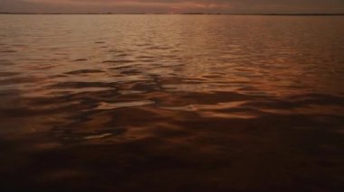 Gün batımında bir nehrin su yüzeyi Yazın dışarıda parlak turuncu yansımalarla