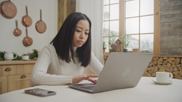 Mujer joven se aburre usando su computadora portátil en su apartamento cocina — Vídeo de stock